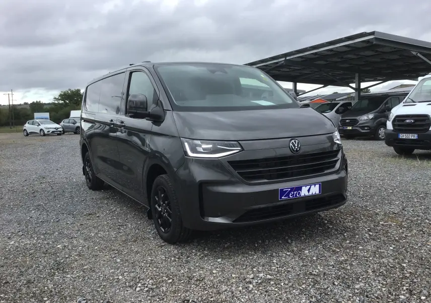 Vue 3/4 avant d'un Volkswagen Transporter T7 gris anthracite avec projecteurs LED Matrix et jantes noires sur parking.