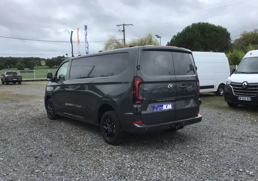 Vue 3/4 arrière droite d'un Volkswagen Transporter T7 gris anthracite avec barres de toit repliables et jantes noires.