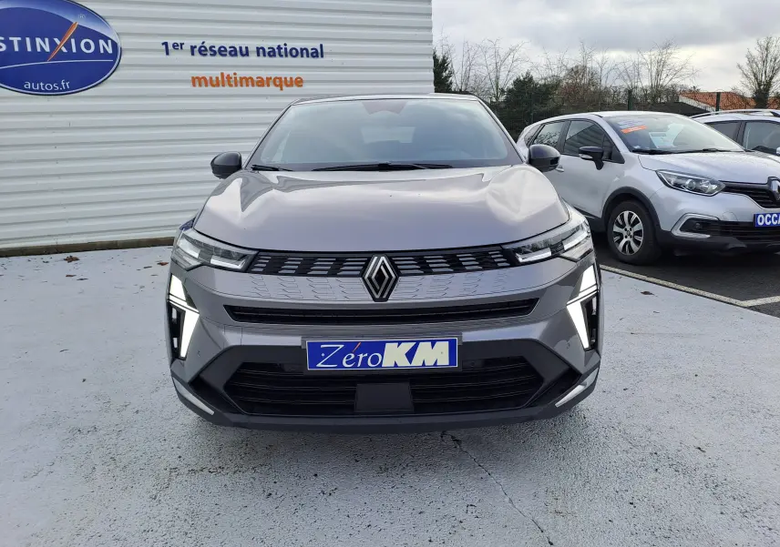 Vue de face d'une Renault Symbioz gris cassiopée avec feux LED allumés sur un parking extérieur.