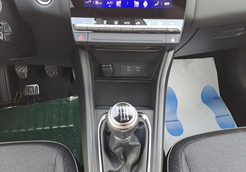 Vue intérieure centrée sur le levier de vitesses manuel de la Renault Symbioz gris Cassiopée avec console et commandes climatisation.