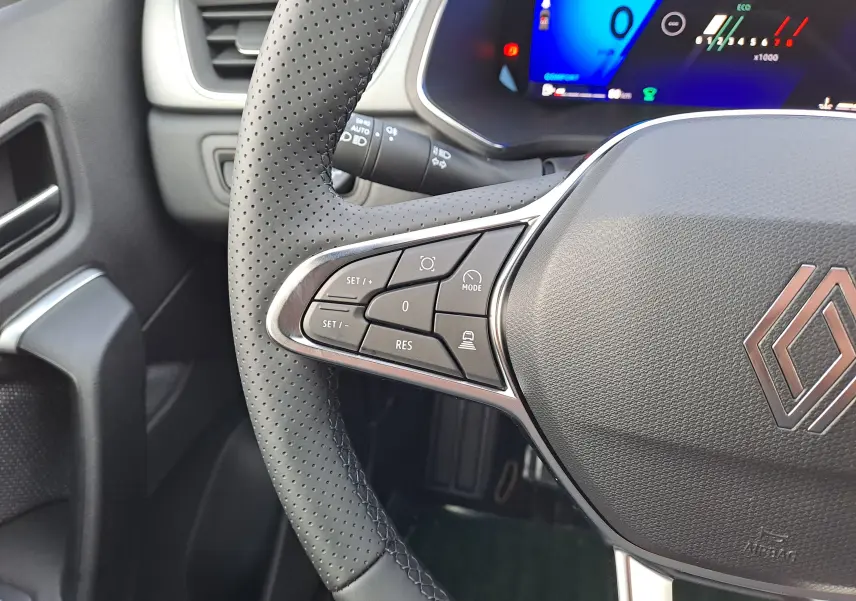 Gros plan sur le volant perforé noir de la Renault Symbioz 2025 avec commandes intégrées et tableau de bord numérique bleu.
