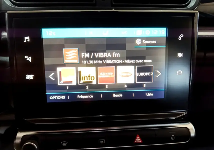 Écran tactile central affichant la radio dans l'habitacle d'une Citroën C3 bleu, vue rapprochée du tableau de bord.