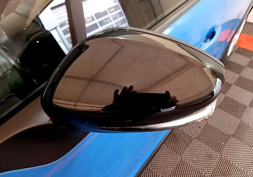 Rétroviseur extérieur noir côté gauche d'une Citroën C3 bleu visible en arrière-plan sur sol damier.