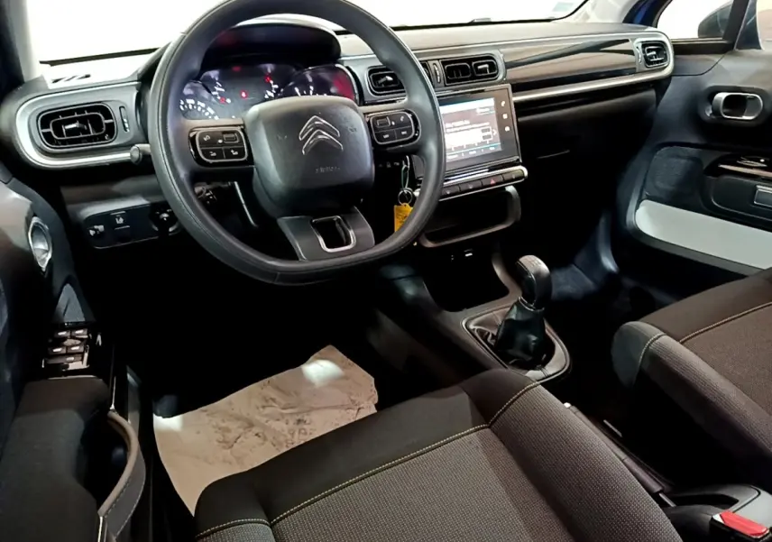 Intérieur avant de la Citroën C3 2017 avec tableau de bord noir, volant multifonctions et boîte manuelle visible côté conducteur.