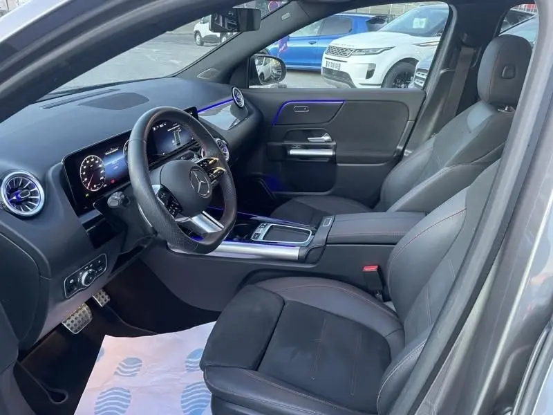 Vue intérieure côté conducteur du Mercedes GLA 250 e AMG Line 2025, avec sellerie cuir noire et éclairage d'ambiance bleu.