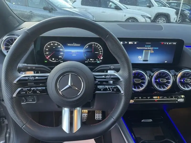 Vue intérieure du tableau de bord et volant Mercedes GLA 250 e AMG Line 2025, avec affichages numériques et éclairage d'ambiance bleu.