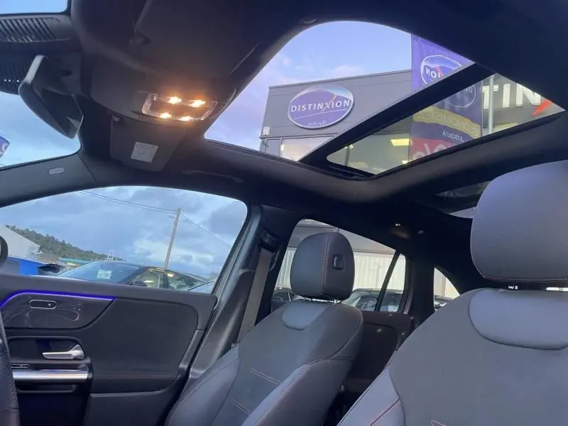 Vue intérieure avant droite du Mercedes GLA 250 e AMG Line 2025 avec toit panoramique et éclairage d'ambiance bleu.