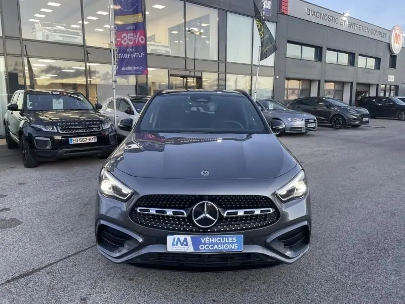 Vue frontale d’un Mercedes GLA 250 e AMG Line gris foncé métal, avec calandre distinctive et feux allumés, en concession.