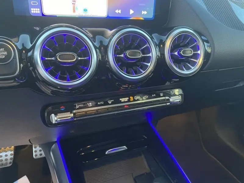 Détail intérieur du tableau de bord du Mercedes GLA 250 e AMG Line 2025, avec aérateurs ronds et éclairage d’ambiance bleu.
