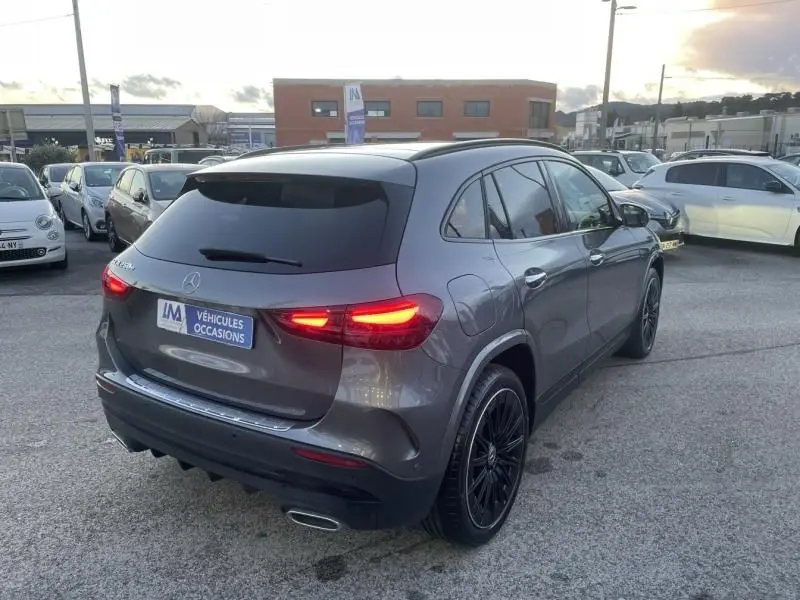 Vue 3/4 arrière droite d’un Mercedes GLA 250 e AMG Line gris foncé métal avec feux arrière allumés et jantes noires.