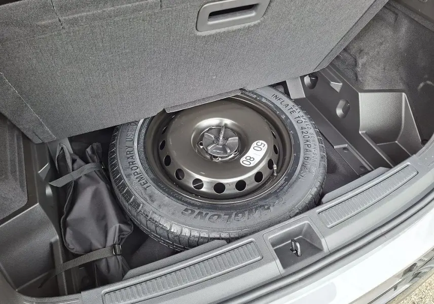 Vue du coffre ouvert du Renault Austral gris schiste, montrant la roue de secours et un sac de rangement noir.