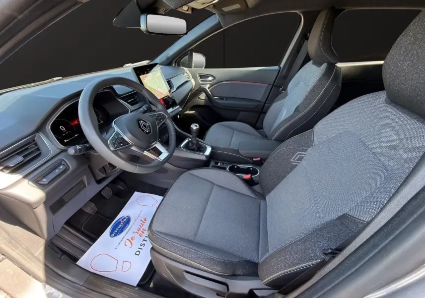 Vue intérieure côté conducteur du Renault Captur TCE 90 Techno 2024, sièges tissu gris Cassiopée avec volant multifonction.