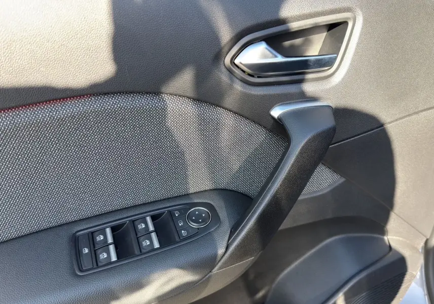 Gros plan sur la porte avant gauche du Renault Captur gris Cassiopée, montrant la poignée, les commandes des vitres et le revêtement tissu noir.