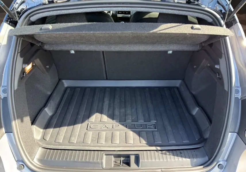 Coffre ouvert vu de l'arrière d'un Renault Captur gris Cassiopée avec tapis de coffre noir marqué Captur.