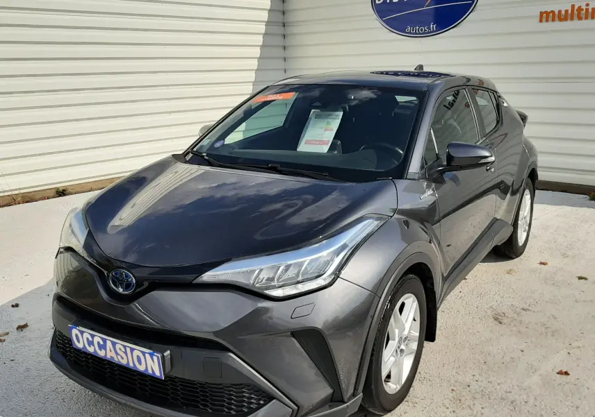 Toyota C-HR 1.8 Hybrid gris atlas métal vu en 3/4 avant droit, avec plaque "OCCASION" et logo Distinxion en arrière-plan.