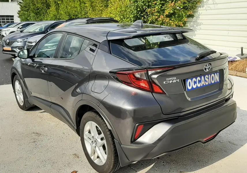 Toyota C-HR 1.8 Hybrid gris atlas métal vu en 3/4 arrière droit avec feux LED et toit noir contrasté.