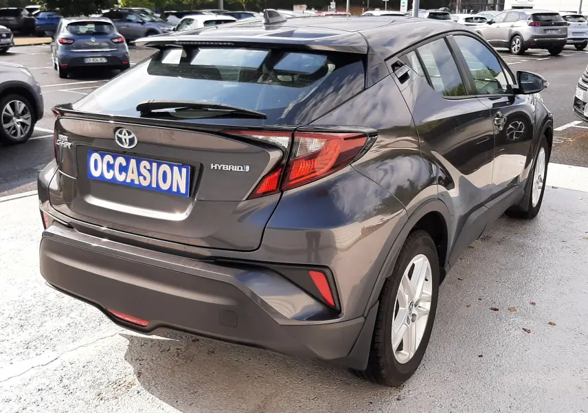 Toyota C-HR 1.8 Hybrid gris atlas métal vu en 3/4 arrière droit, avec feux arrière distinctifs et toit noir.