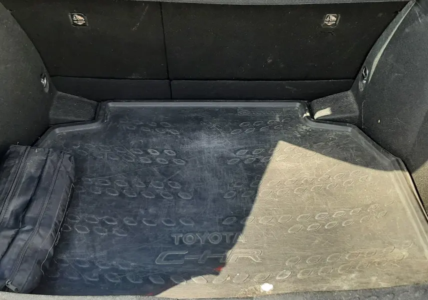Vue du coffre du Toyota C-HR gris atlas, avec tapis de protection marqué du logo et dossier arrière en tissu gris.
