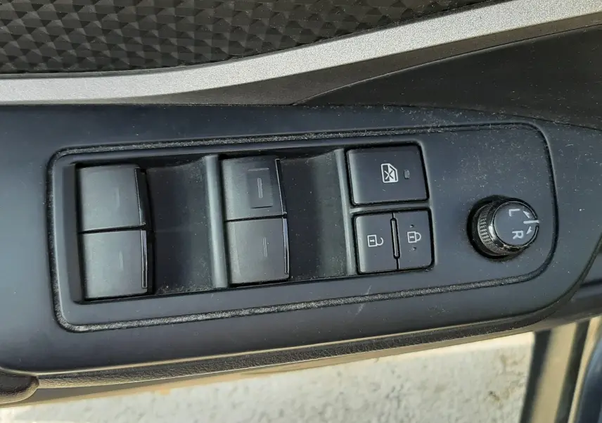 Vue rapprochée des commandes de lève-vitres et réglage des rétroviseurs côté conducteur du Toyota C-HR gris atlas métal.