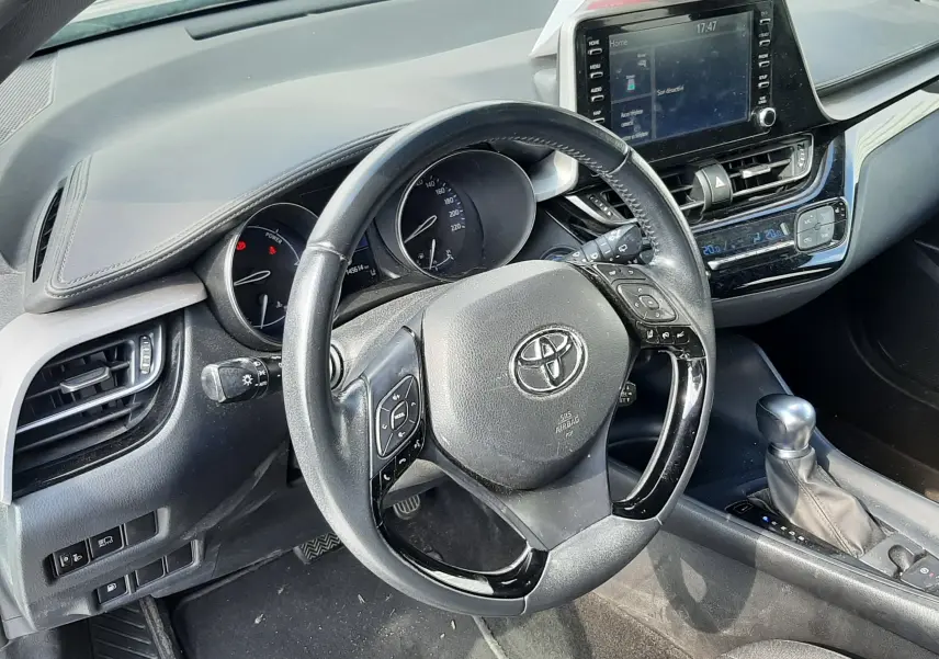 Vue intérieure côté conducteur du Toyota C-HR 1.8 Hybrid 2021, volant multifonction et écran tactile central visibles.