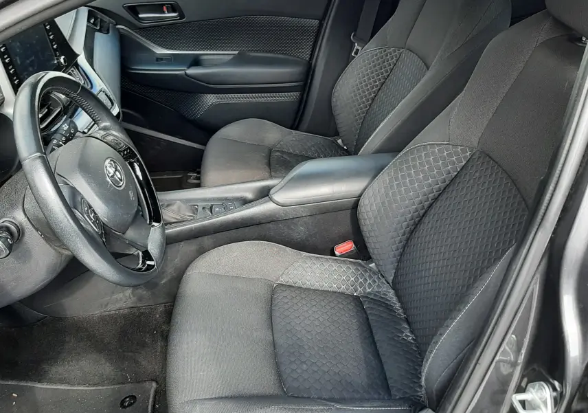 Vue intérieure côté conducteur du Toyota C-HR 1.8 Hybrid gris atlas, sièges tissu gris avec motifs géométriques.