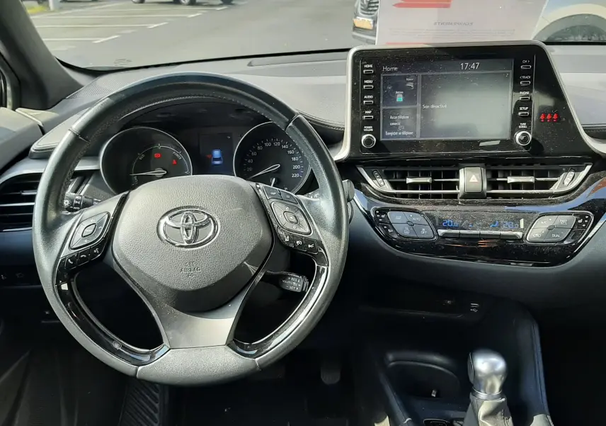 Vue intérieure du tableau de bord et volant du Toyota C-HR 1.8 Hybrid 122 Active, avec écran tactile et levier de boîte auto.