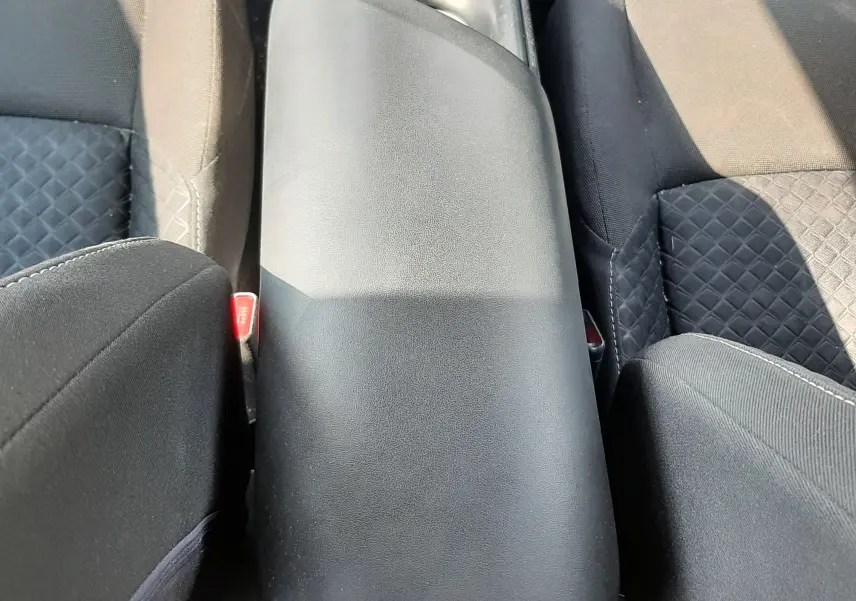Vue plongeante sur l'accoudoir central noir entre les sièges avant en tissu gris du Toyota C-HR 1.8 Hybrid 2021.