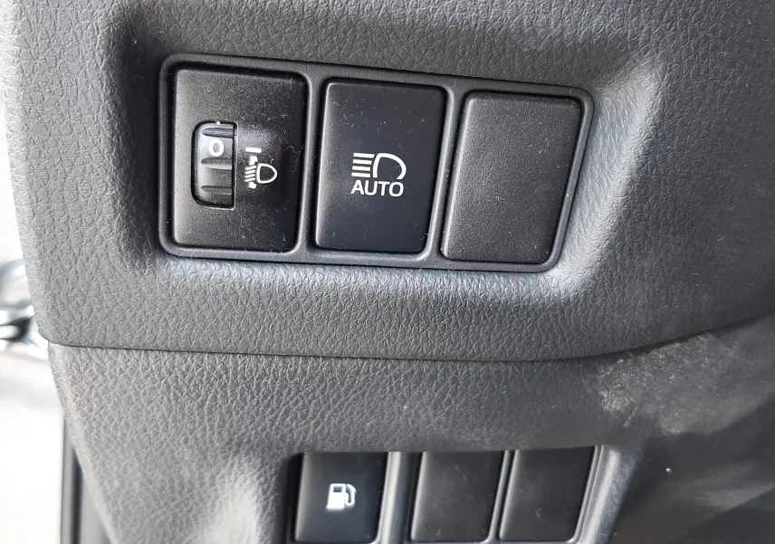Gros plan sur les boutons de réglage des phares et de l'ouverture du réservoir, intérieur gris du Toyota C-HR 1.8 Hybrid.