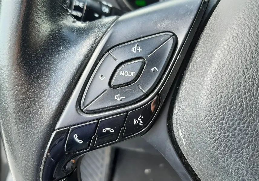 Gros plan sur les commandes multifonctions noires du volant du Toyota C-HR 1.8 Hybrid 2021, intérieur gris.