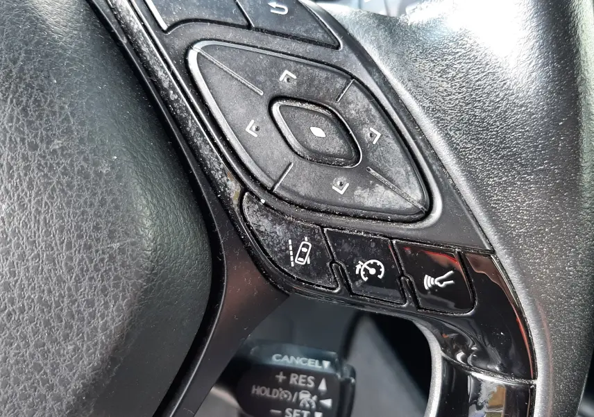 Gros plan sur les commandes multifonctions noires du volant côté gauche du Toyota C-HR gris atlas hybride 2021.