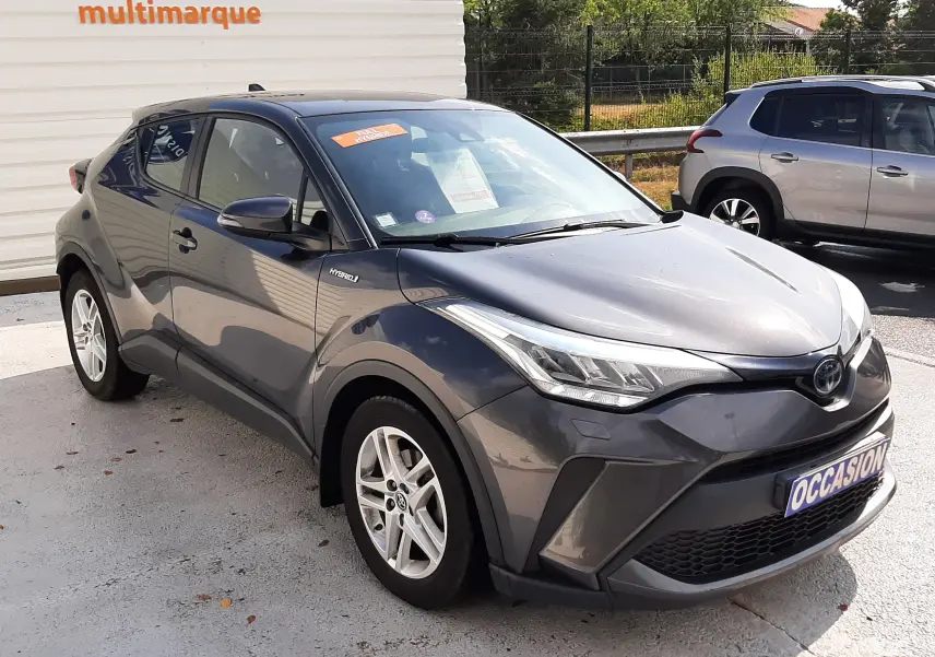 Toyota C-HR 1.8 Hybrid gris atlas métal vu en 3/4 avant droit, avec jantes alliage et feux LED distinctifs.