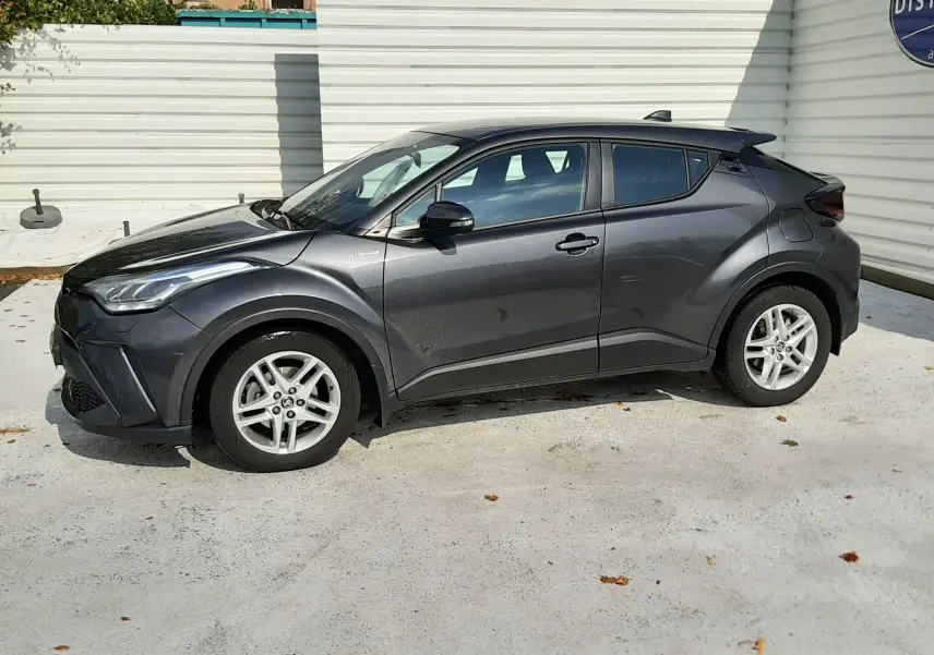 Vue de profil côté gauche d'un Toyota C-HR 1.8 Hybrid gris atlas métal, avec jantes alliage et lignes dynamiques marquées.