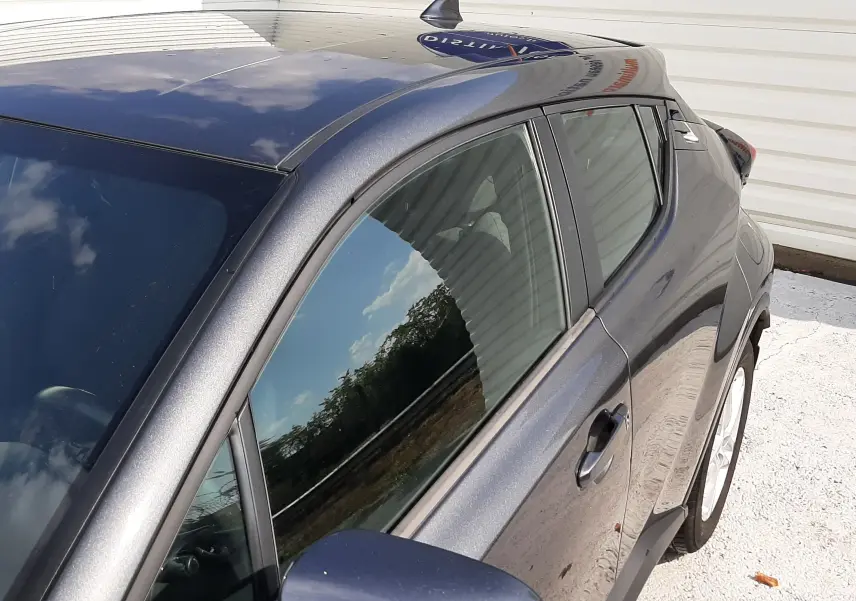 Vue côté gauche avant d'un Toyota C-HR 1.8 Hybrid gris atlas métal, mettant en valeur la peinture métallisée et le rétroviseur.