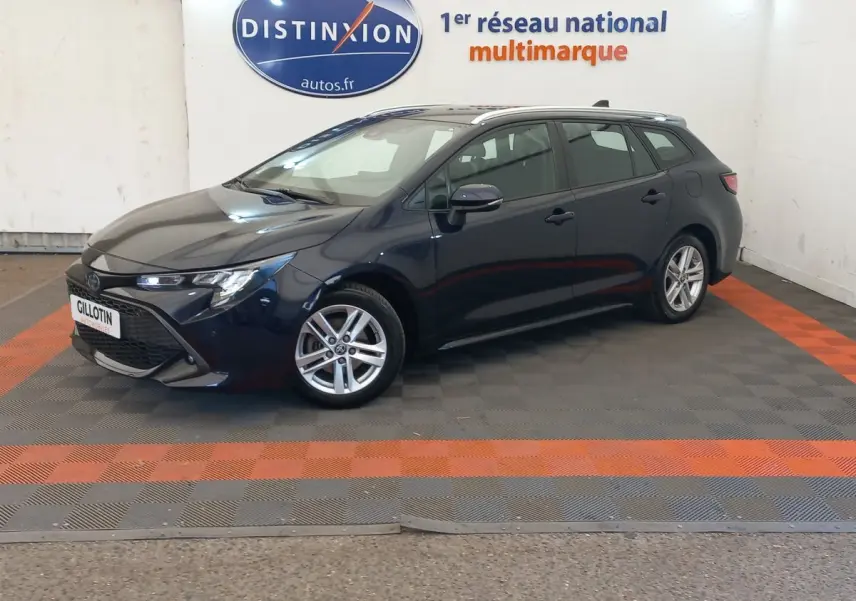Toyota Corolla hybride bleu vue de profil gauche en stationnement intérieur avec jantes alliage et toit ouvrant.