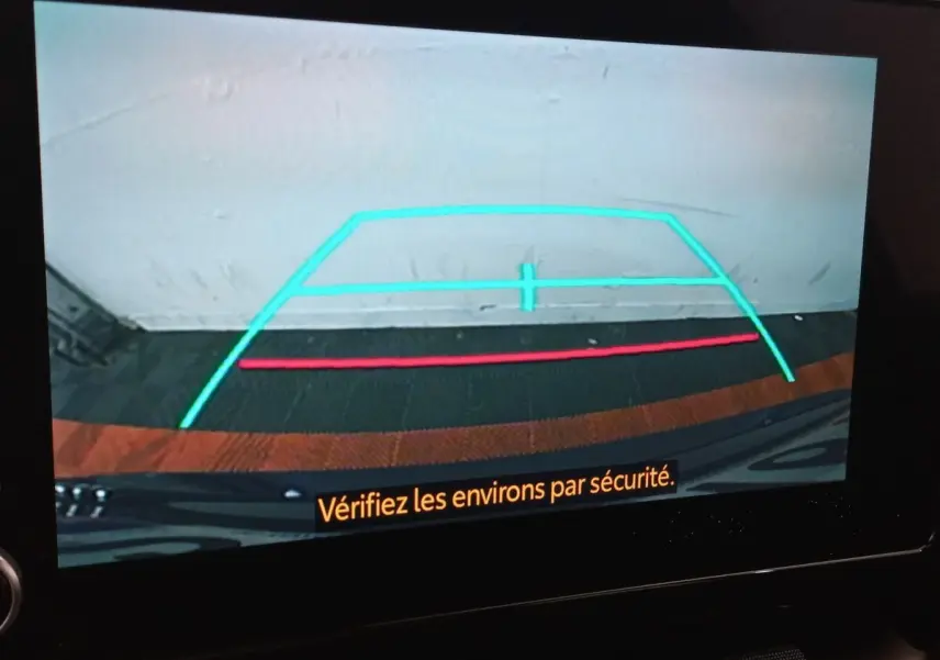 Vue de la caméra de recul d'une Toyota Corolla hybride bleue, avec lignes de guidage colorées à l'écran.