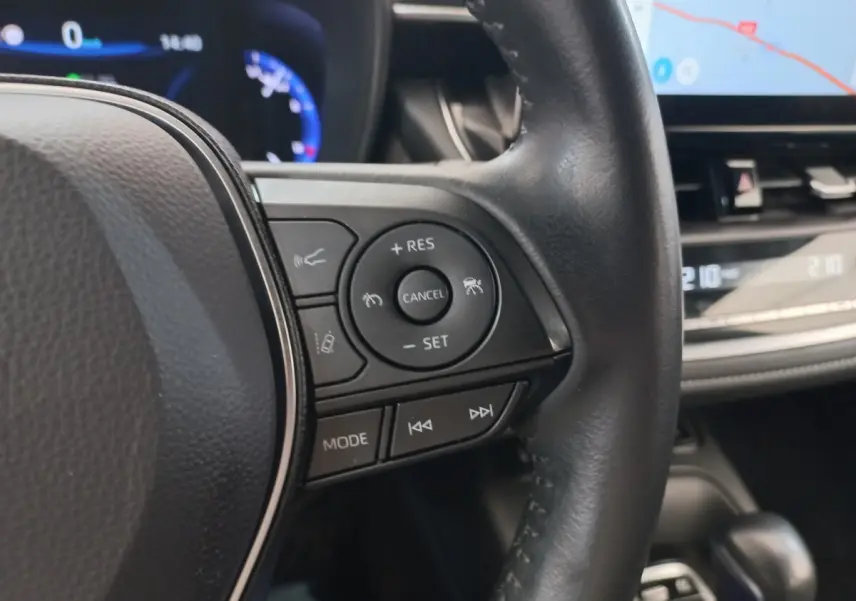 Gros plan sur le volant cuir noir multifonctions de la Toyota Corolla hybride, avec tableau de bord et écran tactile en arrière-plan.