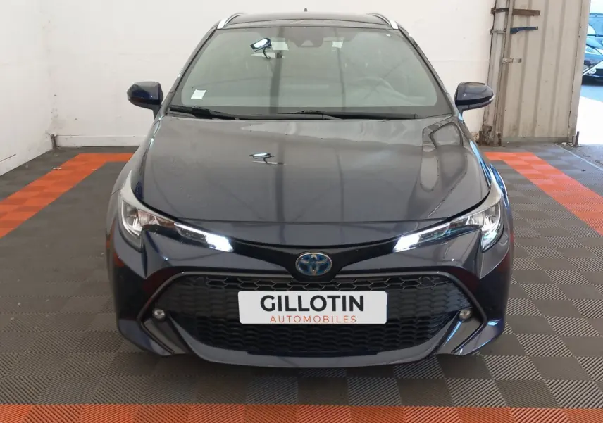 Vue avant d'une Toyota Corolla hybride bleu foncé avec calandre noire et phares LED allumés dans un garage.