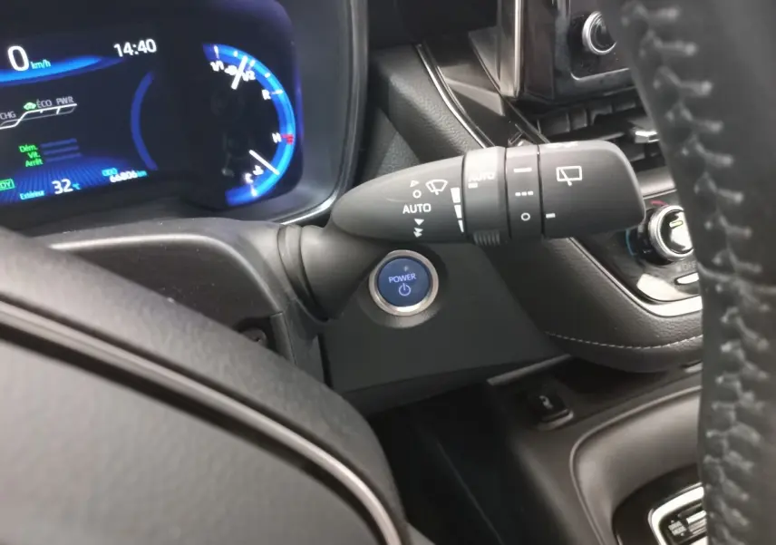 Vue intérieure rapprochée du tableau de bord et du volant cuir d'une Toyota Corolla hybride avec bouton Power bleu et affichage digital.