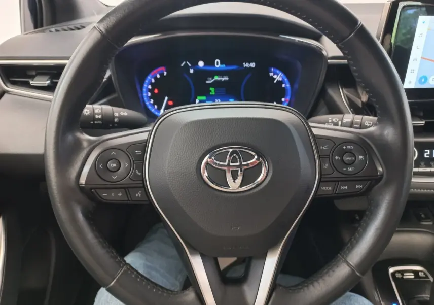 Vue rapprochée du volant cuir multifonctions noir d'une Toyota Corolla hybride 2022 avec tableau de bord digital éclairé.