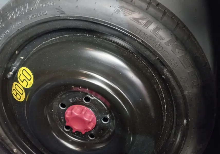 Gros plan sur la roue de secours noire avec bouchon rouge et pneu Falken visible sur une Toyota Corolla hybride bleue.