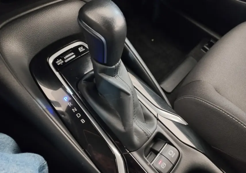 Gros plan sur la console centrale noire avec levier de vitesse automatique en cuir et boutons mode conduite et frein à main électrique.