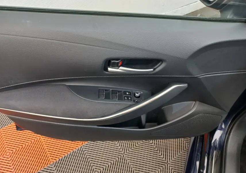 Vue intérieure côté gauche de la porte avant bleu foncé d'une Toyota Corolla hybride avec commandes de vitres et poignée argentée.