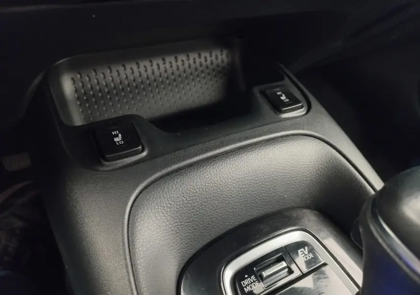 Gros plan sur la console centrale noire de la Toyota Corolla hybride 2022, avec commandes chauffantes et modes de conduite.