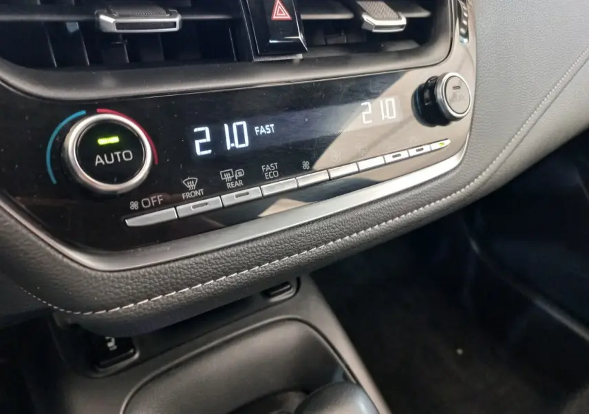 Gros plan sur la console centrale noire de la Toyota Corolla hybride, affichant la climatisation digitale à 21°C.