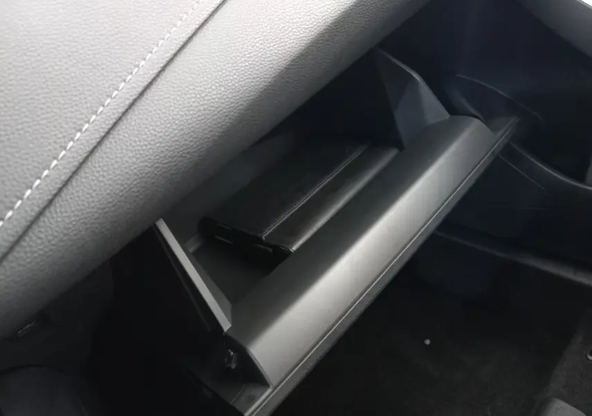Gant de boîte à gants ouvert côté passager avec livret noir dans l’habitacle sombre d’une Toyota Corolla hybride bleue.