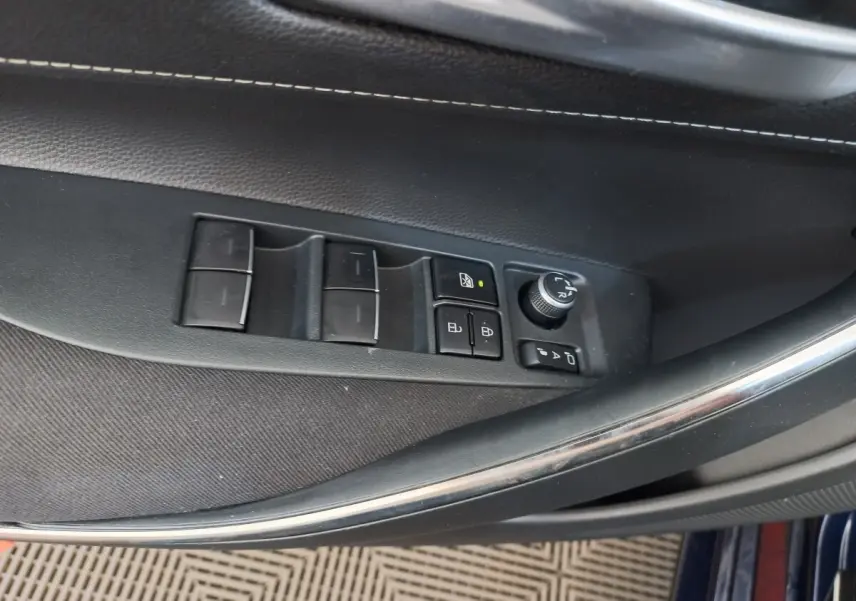 Vue rapprochée des commandes de lève-vitres et rétroviseurs sur la porte côté conducteur d'une Toyota Corolla hybride bleue.