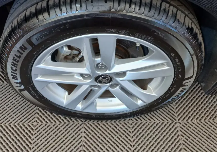 Gros plan sur la jante alliage argentée avec logo Toyota, pneu Michelin, sol en damier sous la roue.