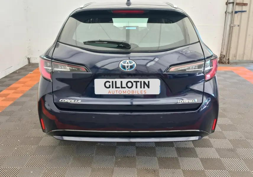 Vue arrière d'une Toyota Corolla hybride bleu foncé avec logo et badges visibles dans un showroom intérieur.