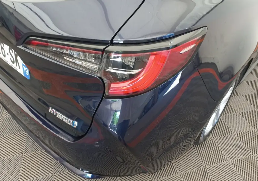 Vue arrière droite de la Toyota Corolla hybride bleu foncé, mettant en valeur le feu arrière et le badge Hybrid.