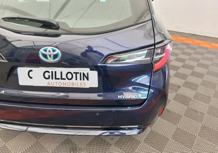 Vue arrière droite d'une Toyota Corolla hybride bleu foncé avec logo Hybrid et plaque d'un concessionnaire.